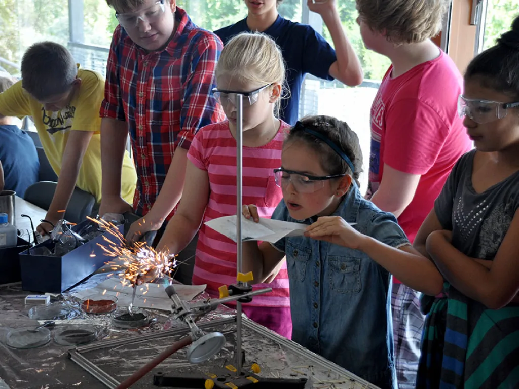 Kinder beobachten mit Schutzbrille einen Versuch mit Funkenflug.